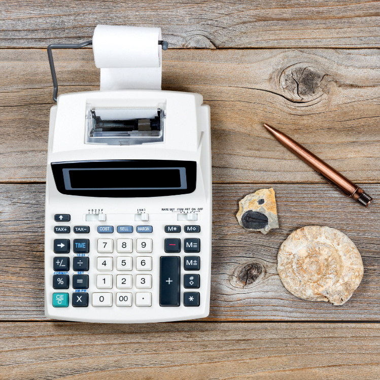 Overhead image of an old adding machine on a wooden table next to a pen and some rocks